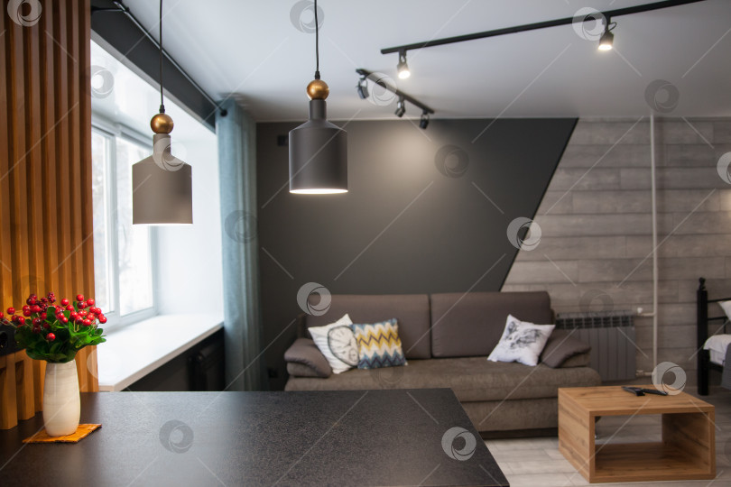 Скачать Серый диван с одеялом, подушкой, деревянным журнальным столиком и растением на деревянном полу в минималистском интерьере. фотосток Ozero