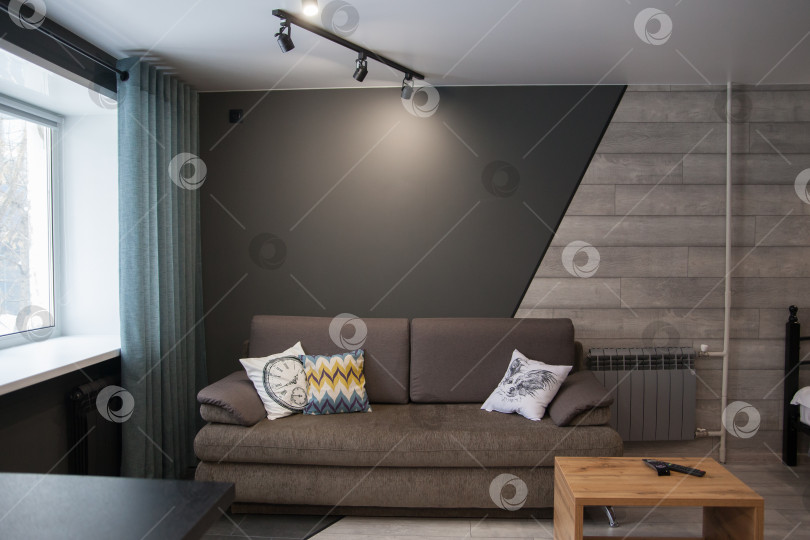 Скачать Серый диван с одеялом, подушкой, деревянным журнальным столиком и растением на деревянном полу в минималистском интерьере. фотосток Ozero