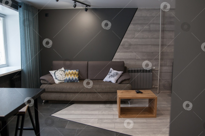 Скачать Серый диван с одеялом, подушкой, деревянным журнальным столиком и растением на деревянном полу в минималистском интерьере. фотосток Ozero