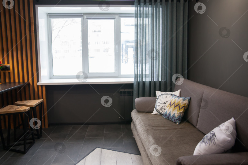 Скачать Серый диван с одеялом, подушкой, деревянным журнальным столиком и растением на деревянном полу в минималистском интерьере. фотосток Ozero