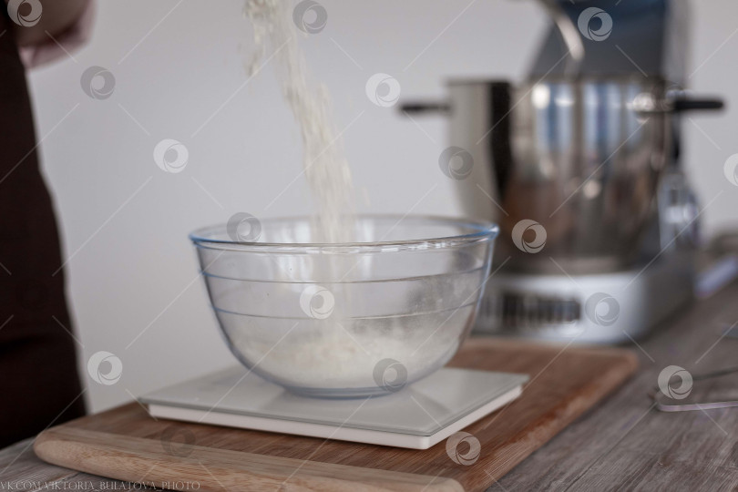 Скачать Насыпьте муку в миску вручную деревянной ложкой. Деревянной ложкой насыпьте пшеничную муку в прозрачную емкость. фотосток Ozero