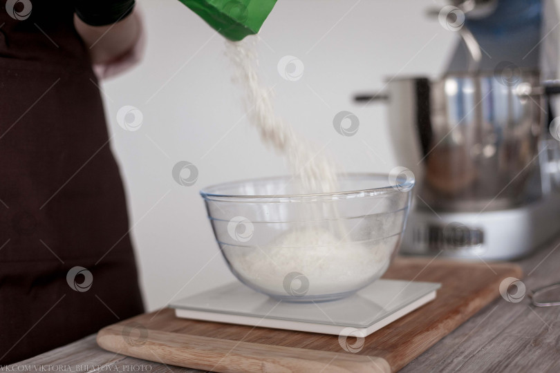 Скачать Насыпьте муку в миску вручную деревянной ложкой. Деревянной ложкой насыпьте пшеничную муку в прозрачную емкость. фотосток Ozero