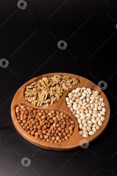 Скачать Деревянная минажница с грецкими орехами, фундуком, фисташками на черном фоне фотосток Ozero
