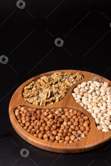 Скачать Деревянная минажница с грецкими орехами, фундуком, фисташками на черном фоне фотосток Ozero
