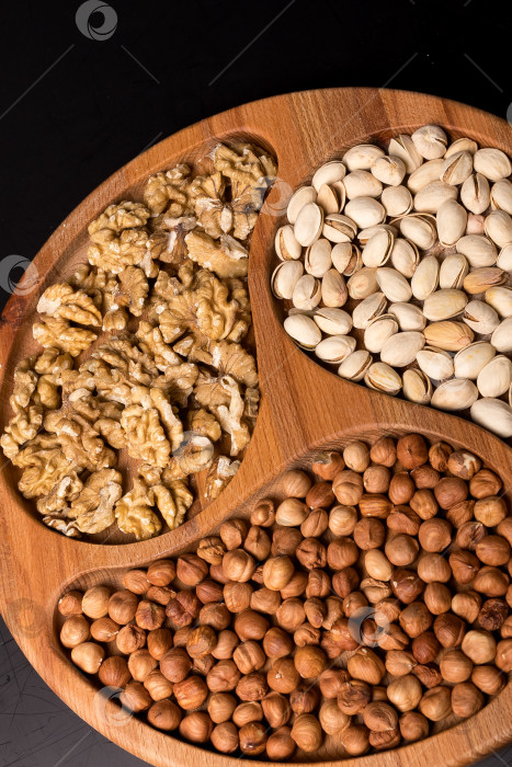 Скачать Деревянная минажница с грецкими орехами, фундуком, фисташками на черном фоне фотосток Ozero