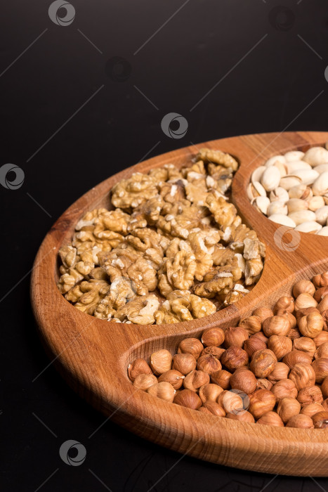 Скачать Деревянная минажница с грецкими орехами, фундуком, фисташками на черном фоне фотосток Ozero