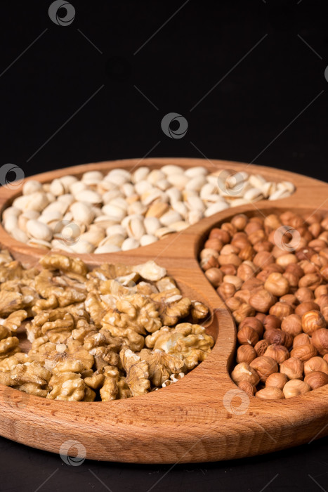 Скачать Деревянная минажница с грецкими орехами, фундуком, фисташками на черном фоне фотосток Ozero