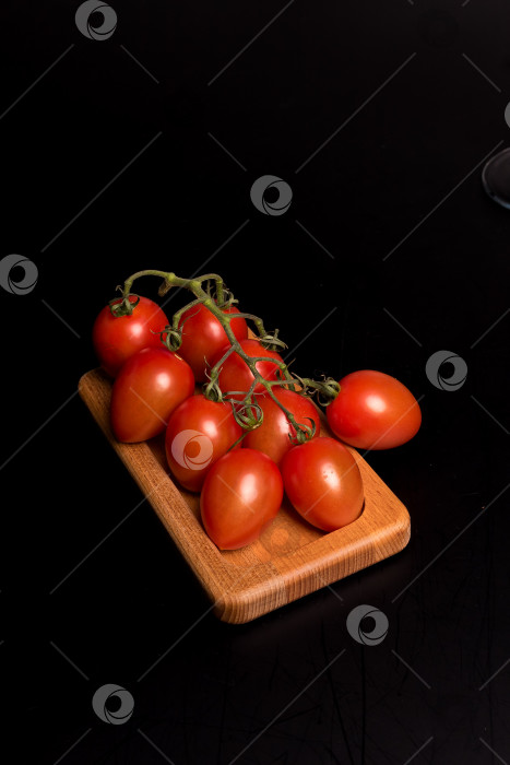 Скачать Свежие красные помидоры черри на деревянной тарелке на черном фоне фотосток Ozero
