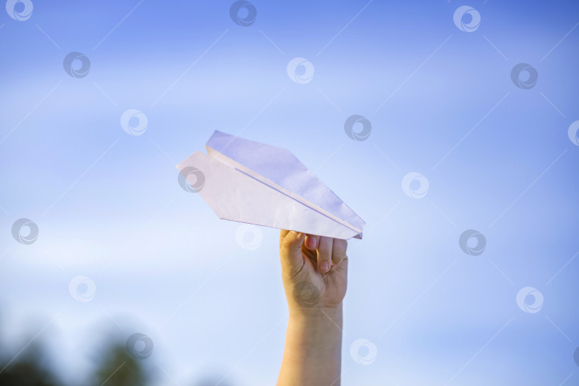 Скачать Рука мальчика держит белый бумажный самолетик на фоне неба. фотосток Ozero