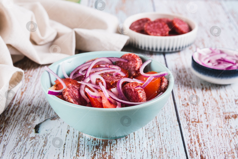 Скачать Delicious salad with chorizo, tomatoes and red onion in a bowl on the table фотосток Ozero