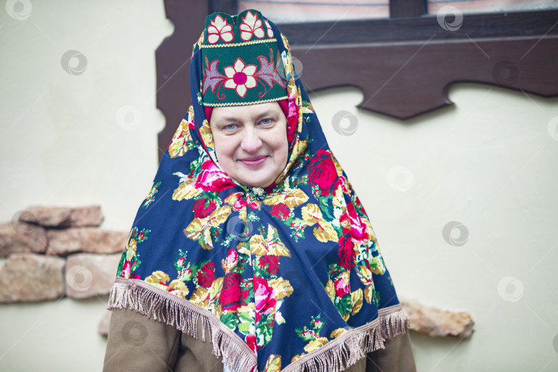 Скачать Пожилая русская женщина в традиционном головном уборе - кокошнике - позирует на фоне деревенского дома. фотосток Ozero