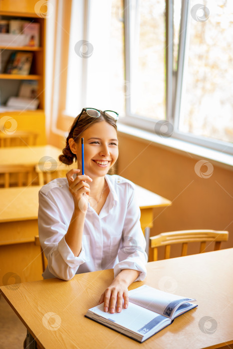 Скачать симпатичная студентка сидит с тетрадью за письменным столом у окна, задумчивый вид фотосток Ozero