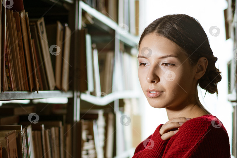 Скачать Молодая женщина смотрит в сторону на фоне книжных полок. фотосток Ozero