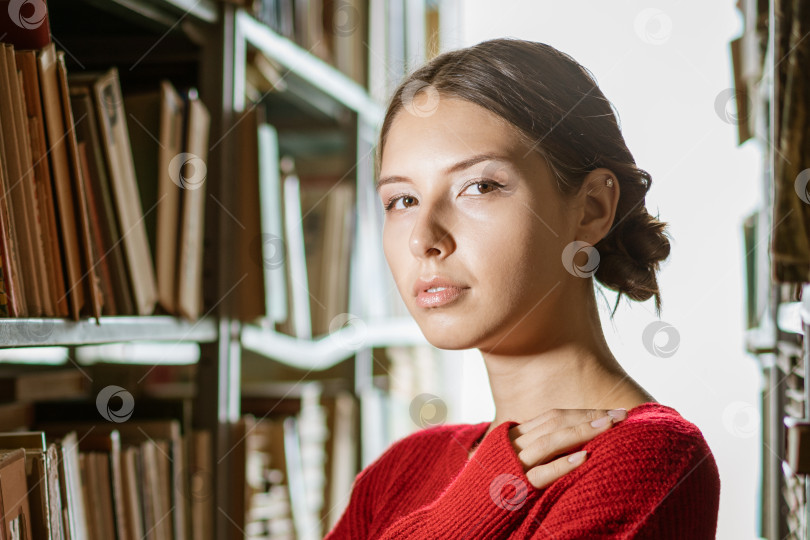 Скачать Портрет девушки, стоящей в библиотеке на фоне книг фотосток Ozero