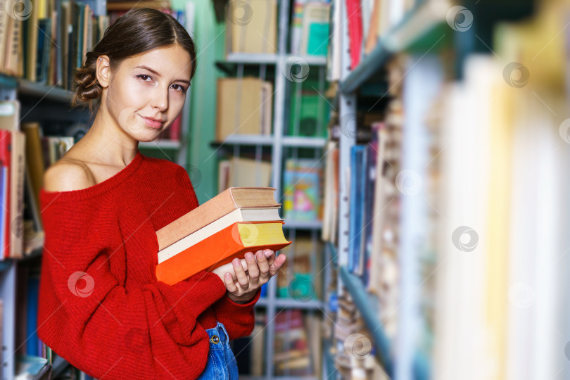 Скачать Студентка стоит в библиотеке с книгами в руках на заднем плане фотосток Ozero