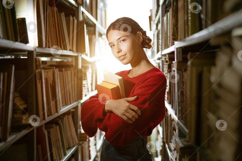 Скачать Девушка держит в руках книгу на фоне библиотеки. фотосток Ozero