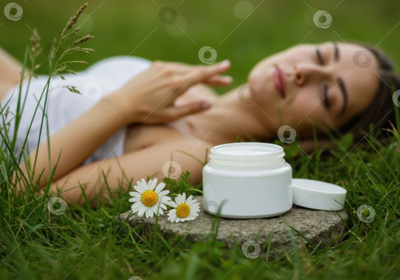 Скачать Женщина лежит на траве, а рядом с ней стоит баночка натуральной косметики, символизирующая естественную красоту и концепцию средств по уходу за кожей. фотосток Ozero