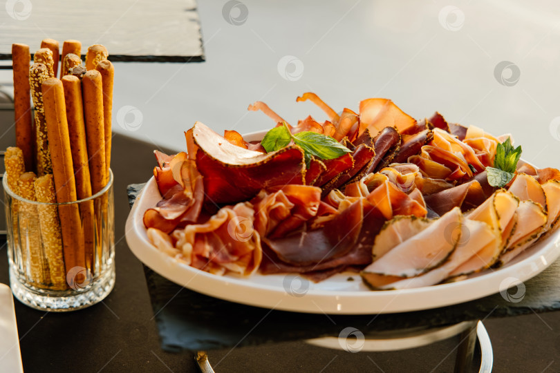 Скачать Изысканная мясная нарезка с деликатесно вяленым мясом, искусно разложенным на блюде, и хрустящими хлебными палочками для гурманов. фотосток Ozero