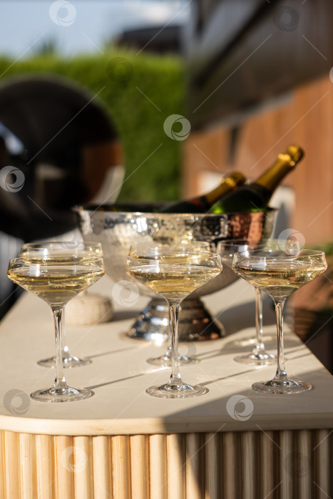 Скачать Красивая композиция из элегантных бокалов для шампанского на мраморном столике с ведерком для льда и бутылками шампанского, отражающими Теплый солнечный свет фотосток Ozero