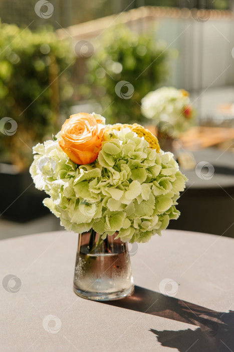 Скачать Красиво оформленное цветочное украшение в центре стола с яркими оранжевыми розами и нежными зелеными гортензиями в стеклянной вазе идеально дополнит любую элегантную обстановку. фотосток Ozero