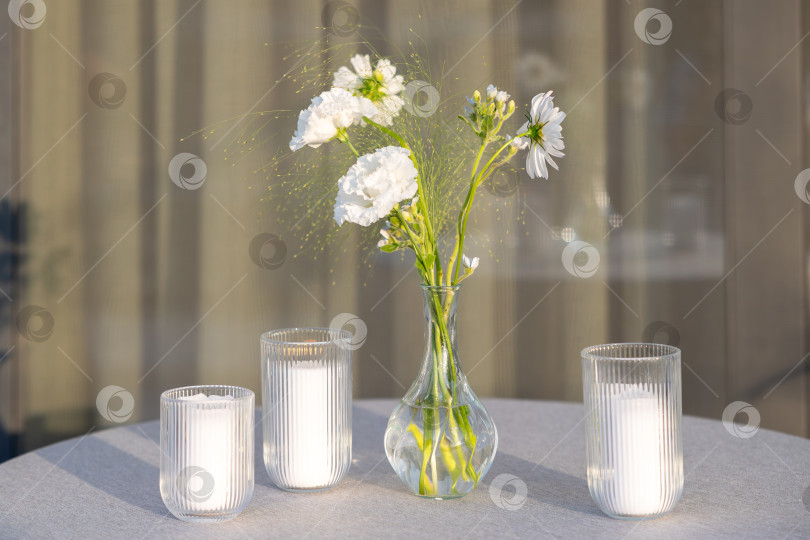 Скачать Безмятежная композиция из белых цветов и свечей на столе идеально подходит для создания умиротворяющей атмосферы в любом помещении с использованием природных элементов. фотосток Ozero