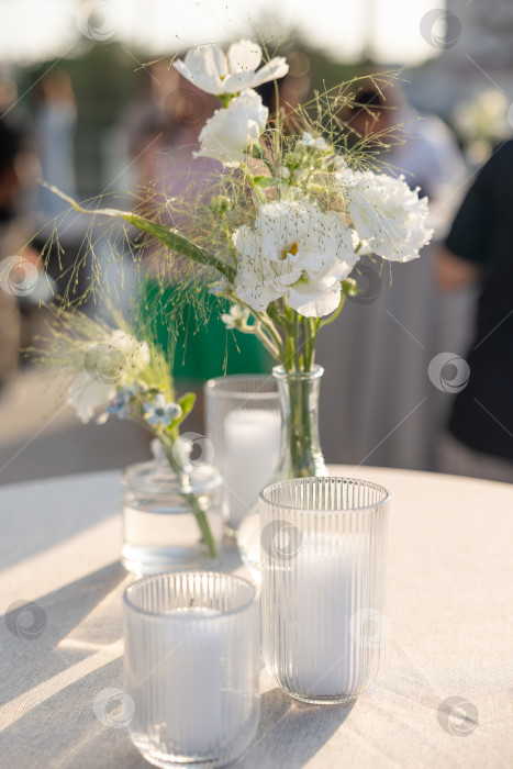 Скачать Элегантная цветочная композиция в стеклянных вазах, расставленная на красиво сервированном столе, создает безмятежную атмосферу для встреч и торжеств фотосток Ozero