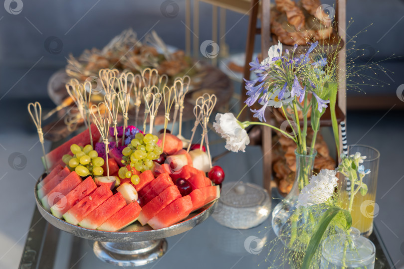 Скачать Красочное блюдо из свежих фруктов и цветочных композиций на элегантном столе, идеально подходящее для летней вечеринки или торжества фотосток Ozero