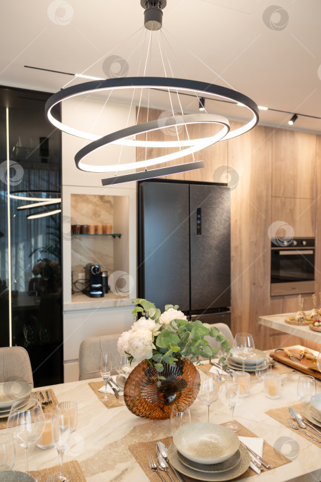 Скачать Современная столовая с минималистским декором, элегантной сервировкой стола и современной люстрой над головой в стильной обстановке кухни фотосток Ozero