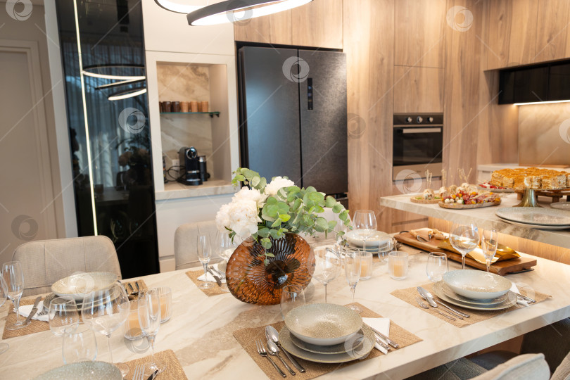 Скачать Элегантный обеденный зал с красиво сервированным столом, украшенным цветами в центре, и современными кухонными элементами идеально подходит для проведения встреч и торжеств. фотосток Ozero