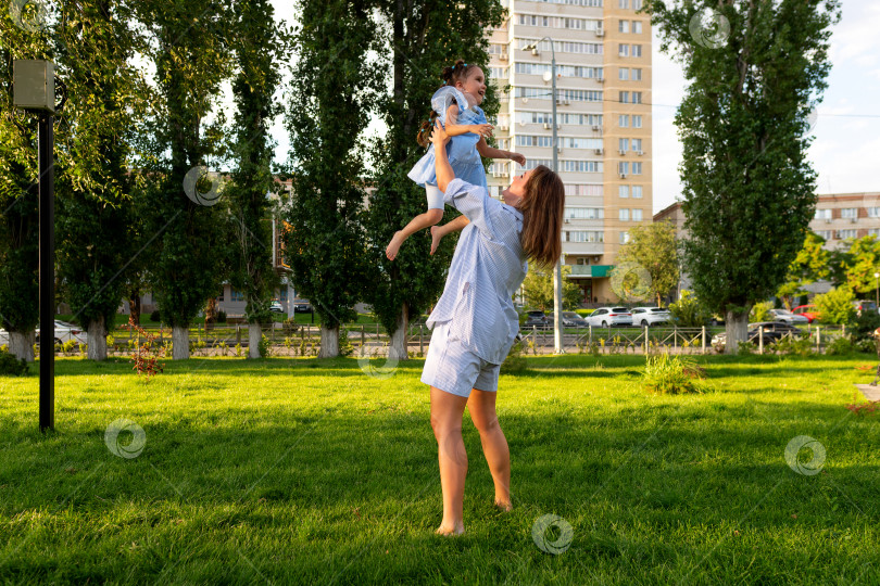 Скачать Мать поднимает смеющуюся дочь высоко над лужайкой грин-парка фотосток Ozero