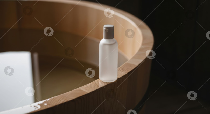 Скачать Белая косметическая бутылочка на деревянном бортике ванны с водой для создания макетов косметических средств. Концепция натурального ухода за кожей и спа-салона. фотосток Ozero