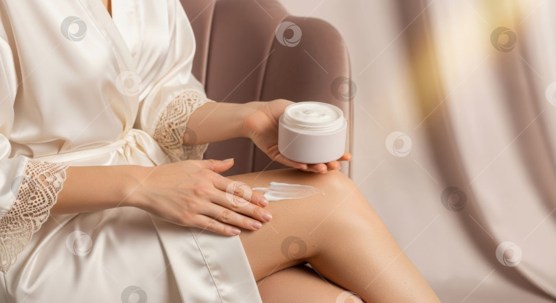 Скачать Женщина наносит белый лосьон для тела для ухода за кожей. Женская рука наносит крем на ноги. Увлажнение для красоты и здоровья. фотосток Ozero