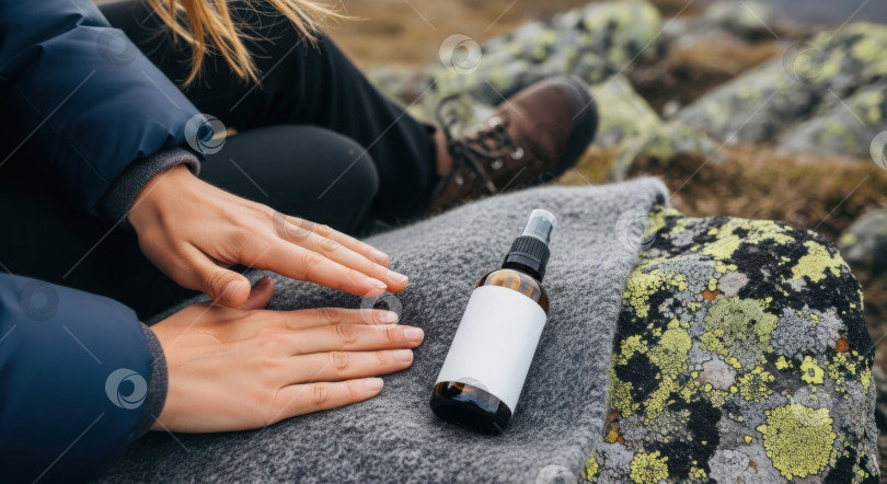 Скачать Женщина с каштановыми волосами сидит на одеяле рядом с заготовкой косметического флакона для изготовления макета этикетки на заказ для рекламы косметических средств или медицинских услуг. фотосток Ozero