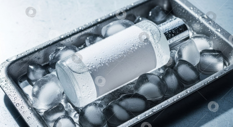 Скачать Прозрачная стеклянная бутылка с пустой этикеткой и капельками воды охлаждается на кубиках льда в металлическом контейнере. Концепция макета. фотосток Ozero