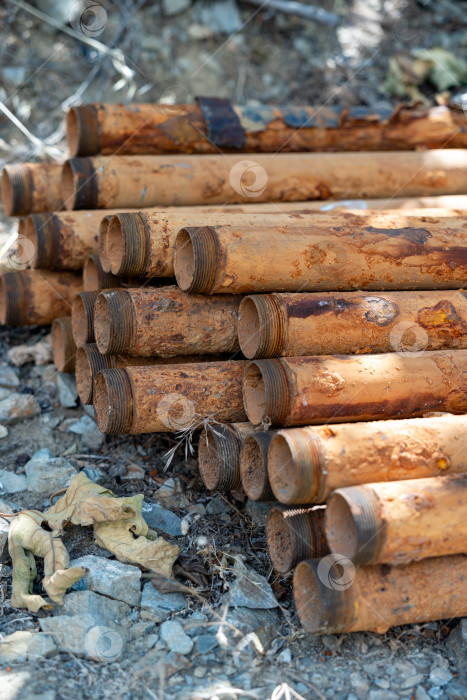 Скачать Крупный план ржавых металлических труб, сложенных на Земле посреди естественной обстановки на открытом воздухе с камнями и сухими листьями. фотосток Ozero