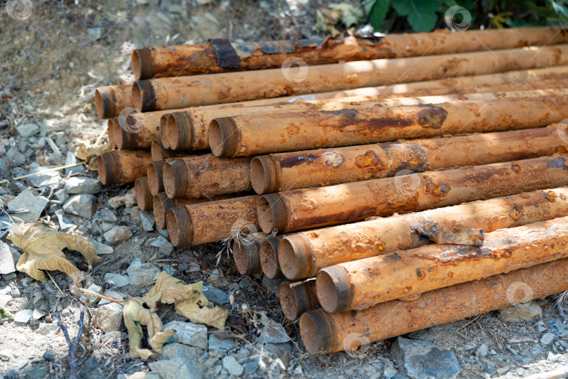 Скачать Коллекция ржавых металлических труб, сложенных штабелем на земле в окружении природных элементов в сельской местности фотосток Ozero