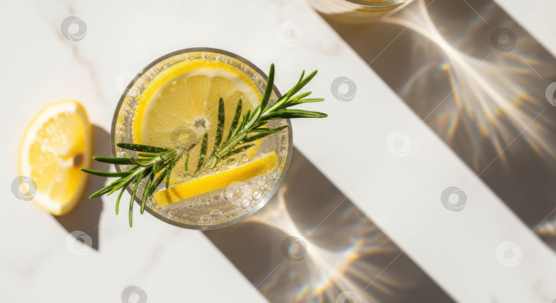 Скачать Вид сверху на освежающий летний напиток с лимоном и розмарином. Яркий солнечный свет в сочетании с эстетичными тенями для маркетинга напитков. фотосток Ozero