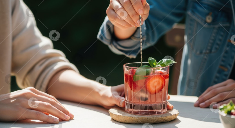 Скачать Женщина помешивает клубнично-базиликовый коктейль в бокале. Освежающий летний напиток для отдыха на свежем воздухе или торжественного мероприятия. фотосток Ozero