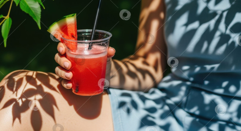 Скачать Женщина держит в руках свежий арбузный коктейль с ломтиком арбуза в пластиковом стаканчике, идеально подходящий для летнего напитка. фотосток Ozero
