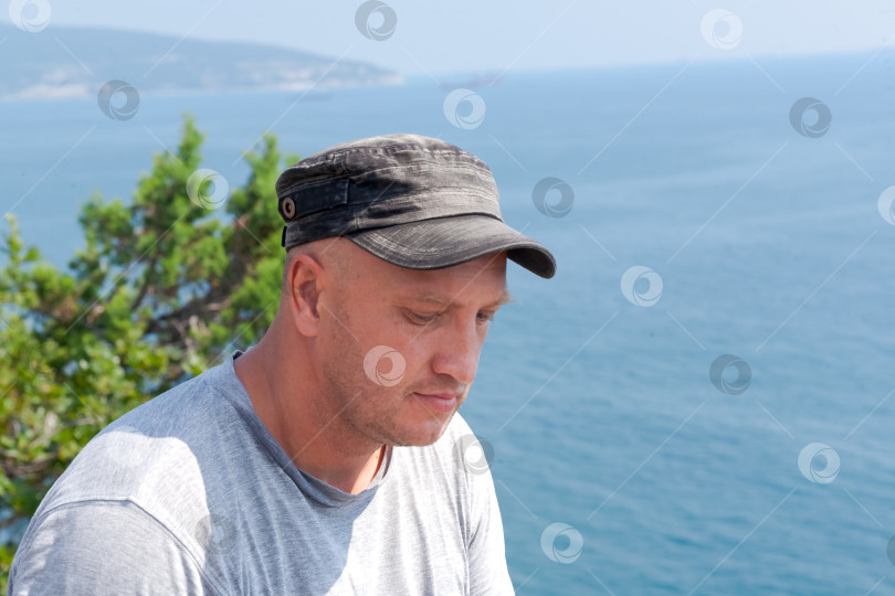 Скачать Мужчина в шляпе и серой рубашке сидит на скале с видом на океан фотосток Ozero