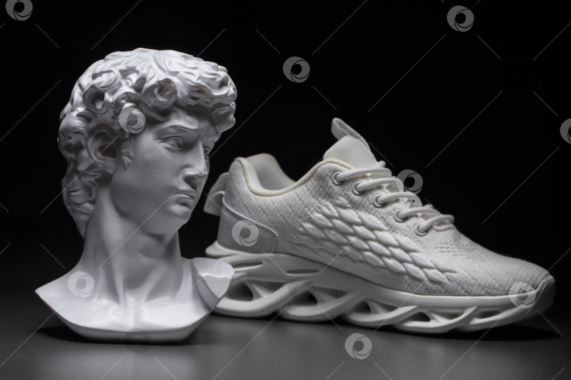 Скачать На темном фоне - гипсовая голова Аполлона и фактурная белая кроссовка. фотосток Ozero