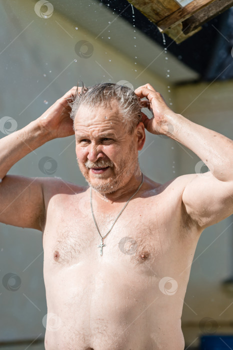 Скачать Мужчина с обнаженной грудью остывает в жару под струями летнего дождя, стекающими с крыши фотосток Ozero