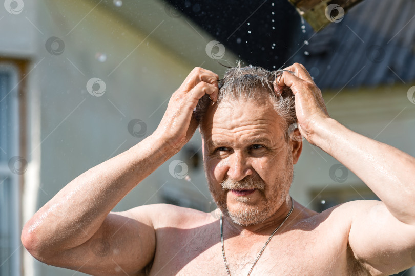 Скачать Мужчина с обнаженной грудью остывает в жару под струями летнего дождя, стекающими с крыши фотосток Ozero