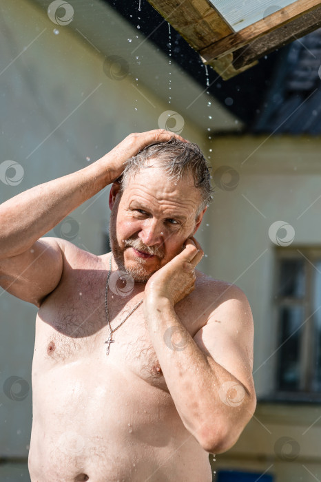 Скачать Мужчина с обнаженной грудью остывает в жару под струями летнего дождя, стекающими с крыши фотосток Ozero