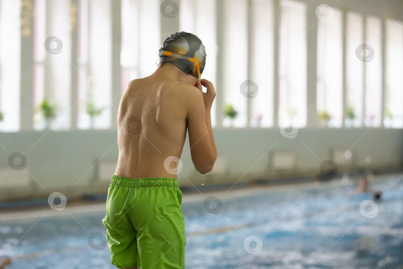 Скачать Мальчик в плавательной шапочке и защитных очках ныряет в спортивный бассейн. фотосток Ozero