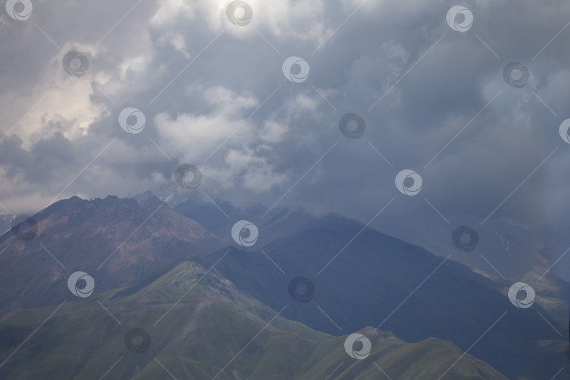 Скачать Мрачный атмосферный сюрреалистический пейзаж с темной скалистой горной вершиной в низких облаках на сером облачном небе. Серое низкое облако на высоком пике. Высокая черная скала в низких облаках. Сюрреалистические мрачные горы. фотосток Ozero