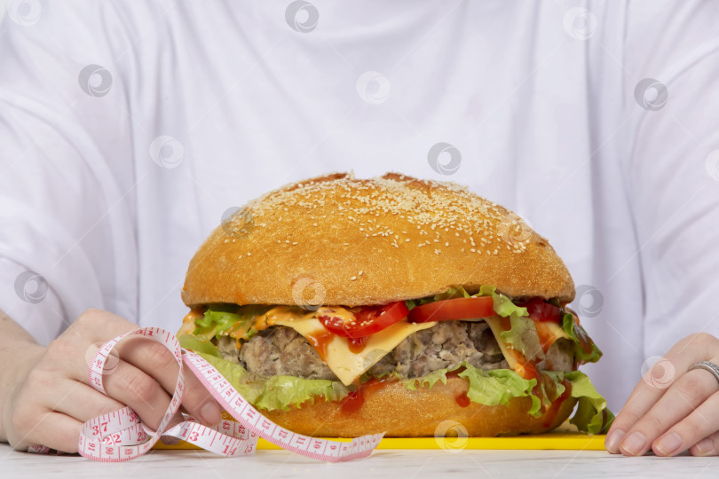 Скачать Рулетка для приготовления большого бургера на столе на фоне женских рук. Концепция диеты и устранения лишних калорий. фотосток Ozero