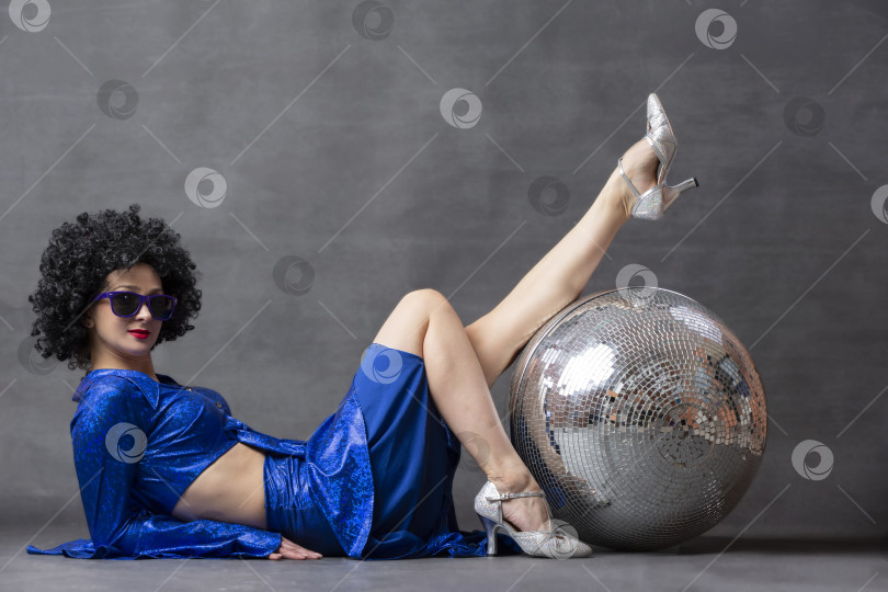 Скачать Девушка с диско-шаром в африканском парике на сером фоне. Стиль диско семидесятых или восьмидесятых годов. фотосток Ozero