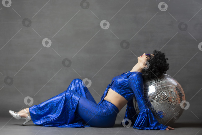 Скачать Девушка с диско-шаром в африканском парике на сером фоне. Стиль диско семидесятых или восьмидесятых годов. фотосток Ozero