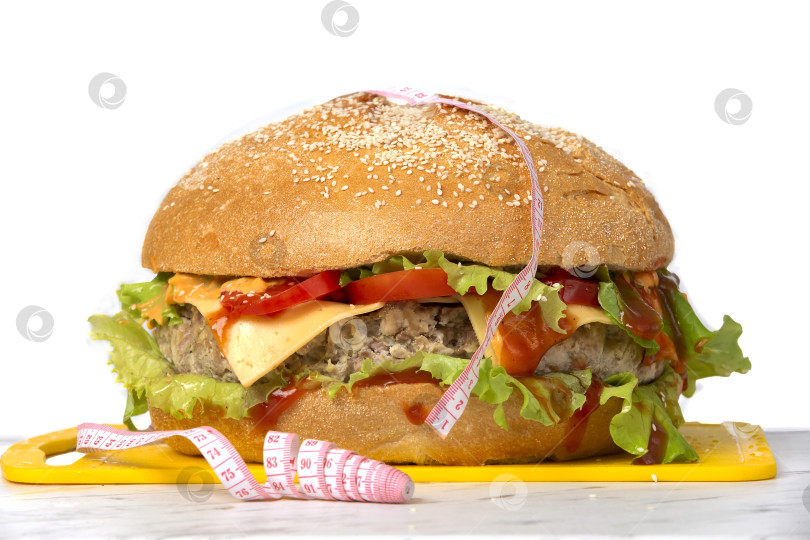 Скачать Гамбургер, обернутый рулеткой, на белом фоне. Концепция похудения. фотосток Ozero